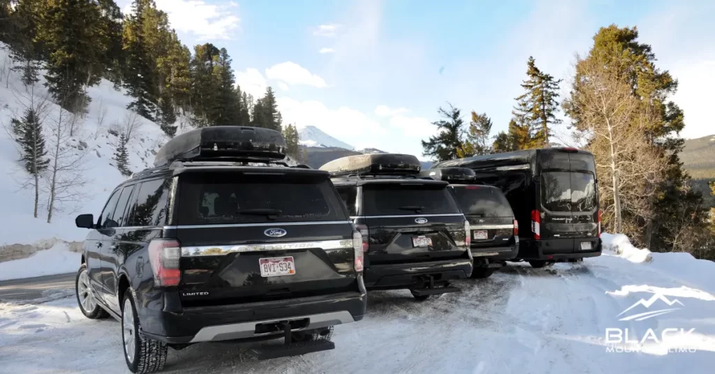 Four black SUVs parked on a snowy road in Colorado.